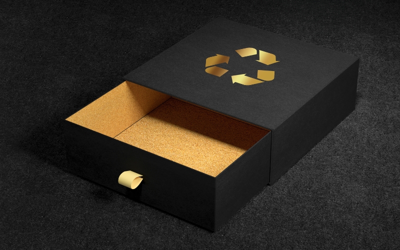 Packaging sostenibile alternative Una lussuosa scatola nera con cassetto scorrevole e il simbolo universale del riciclo in rilievo dorato, che simboleggia il packaging sostenibile.